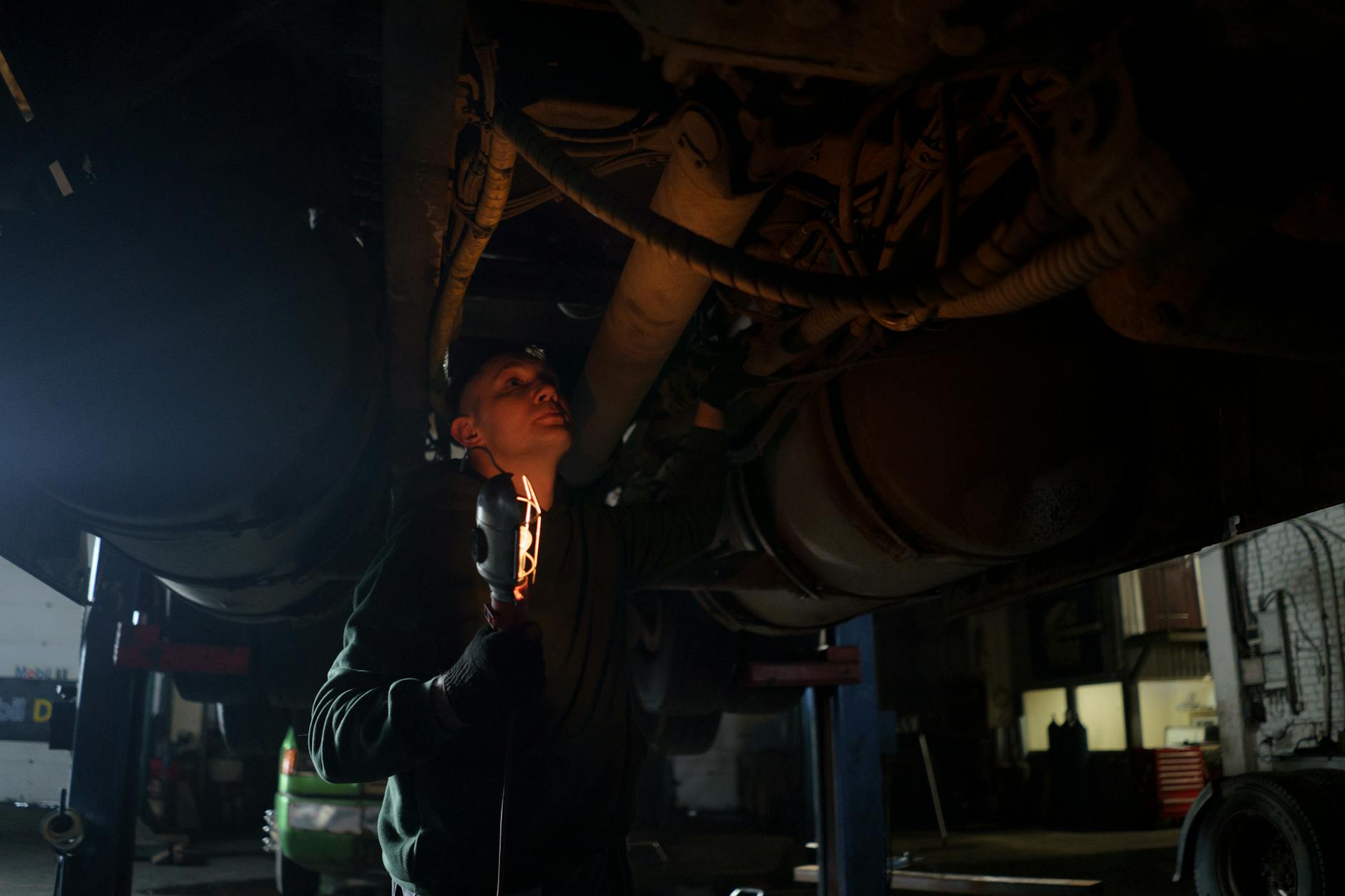 Mechanik z lampą inspekcyjną ogląda podwozie auta w ciemnym warsztacie