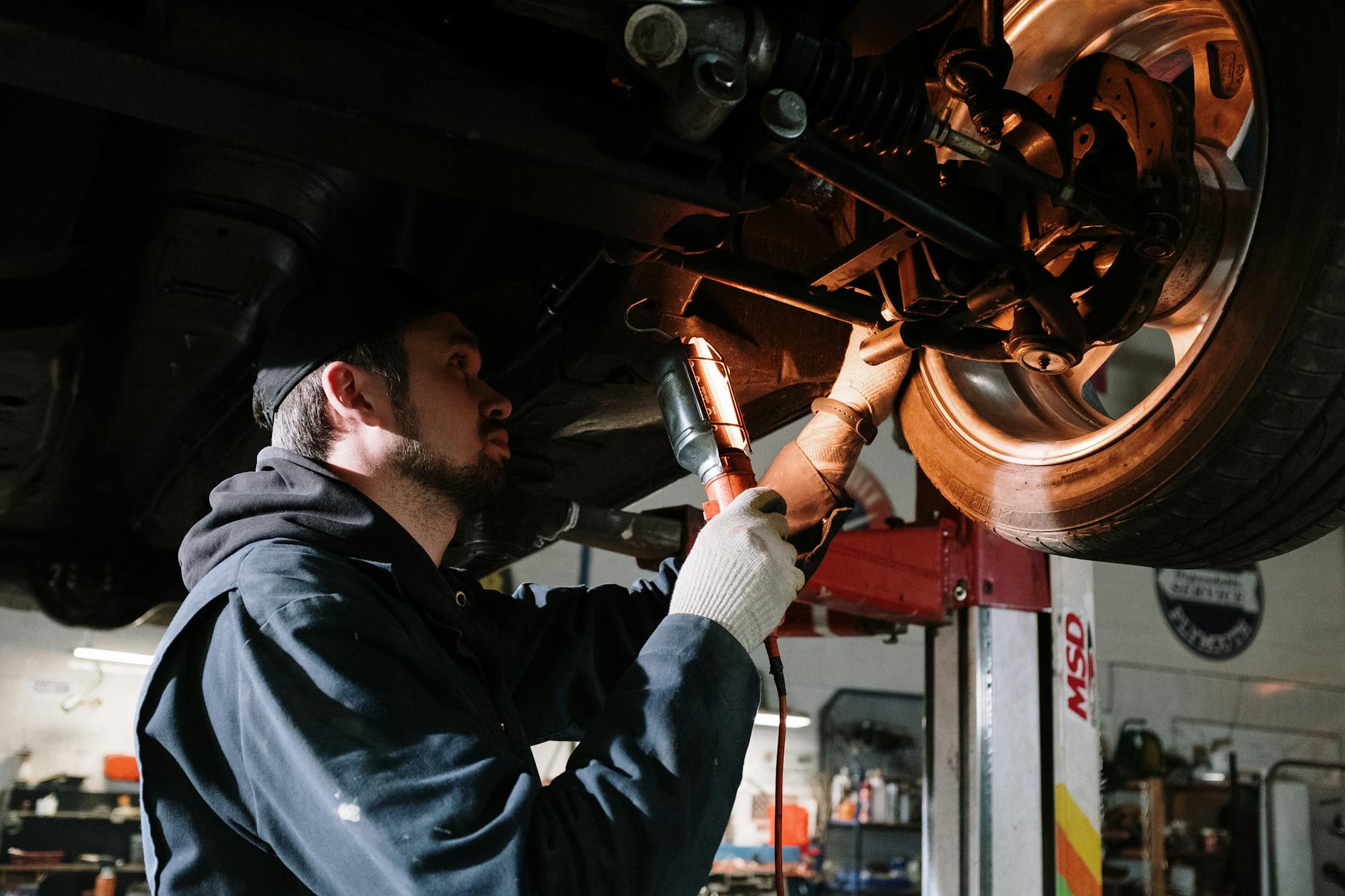 Mechanik ogląda podwozie auta na podnośniku w warsztacie Mechanik ogląda podwozie auta na podnośniku w warsztacie