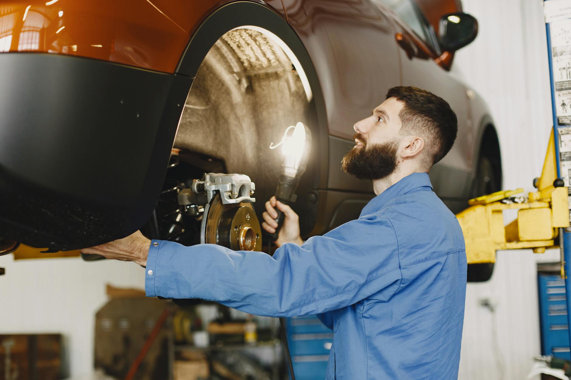 Mechanik w niebieskim kombinezonie sprawdza hamulce auta w warsztacie