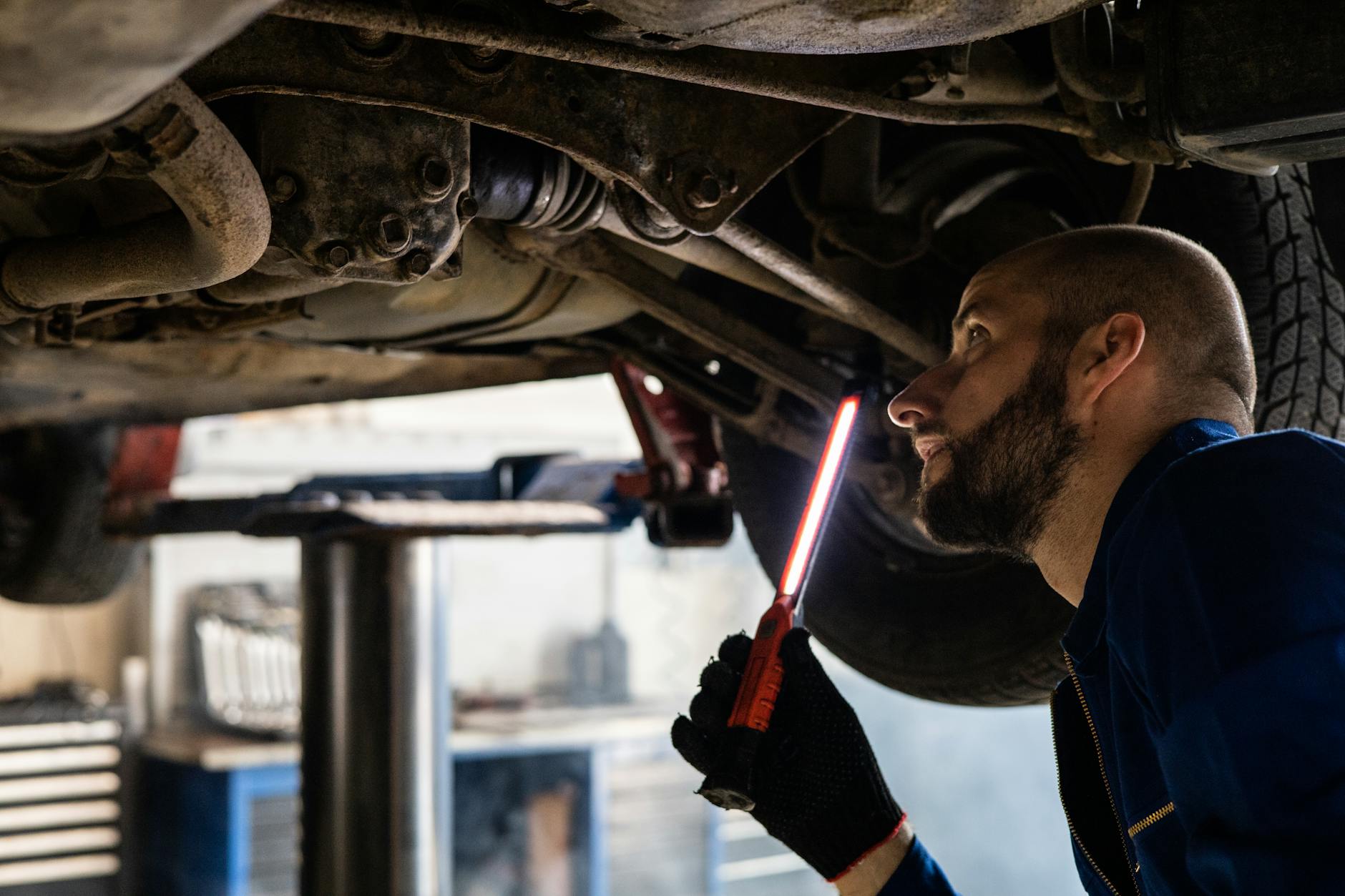 Mechanik z latarką sprawdza podwozie samochodu na podnośniku